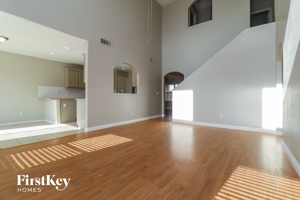 A spacious room with wooden flooring and a staircase on the right side.