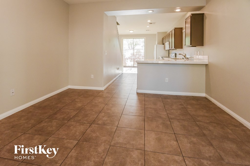 A spacious room with brown tiled flooring and a kitchen area in the background.