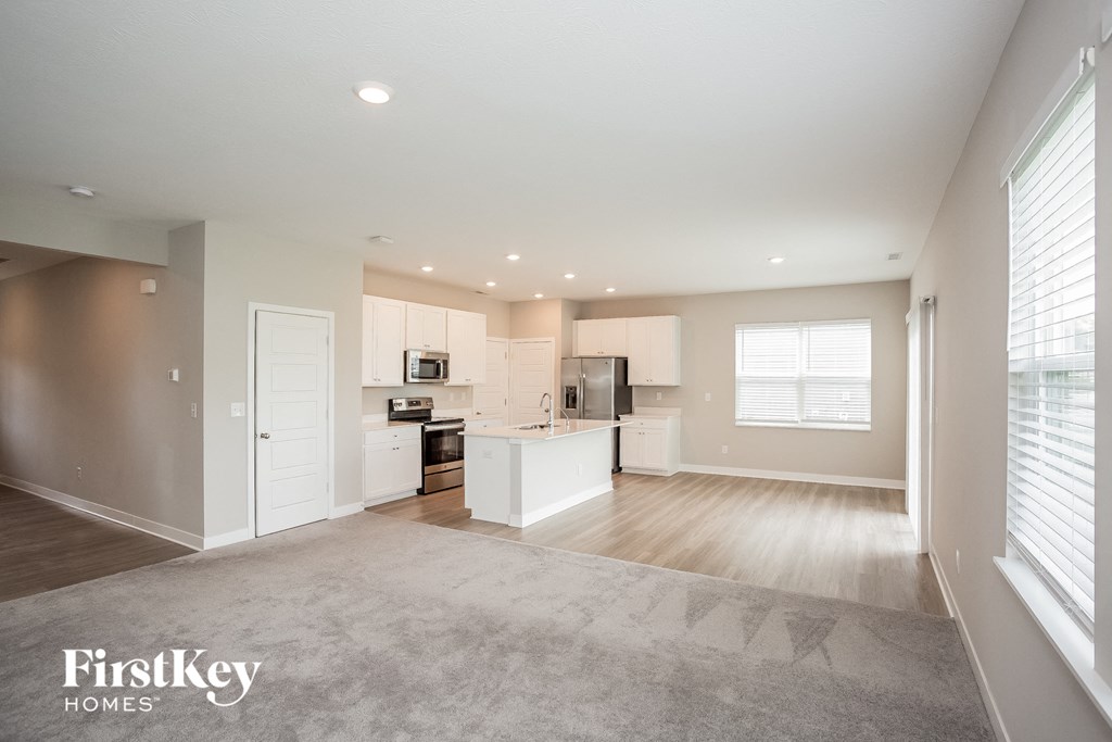 A spacious kitchen and living room with a grey carpet.