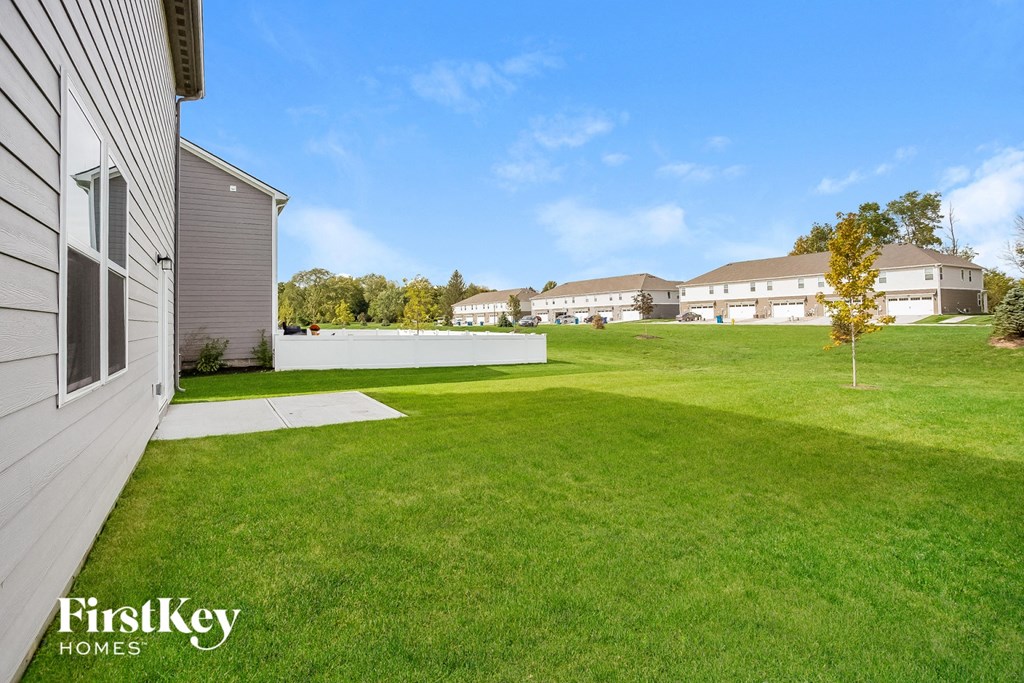 A grassy yard with a house and trees in the background.