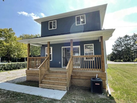 a blue house with a porch and a trash can in front of it