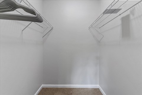 a walk in closet with white walls and a wire rack on the wall