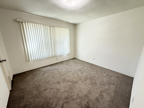 A room with a carpeted floor and a window with blinds.