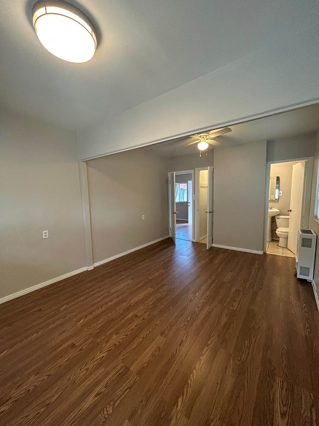 an empty living room with wood flooring and a door to a bathroom