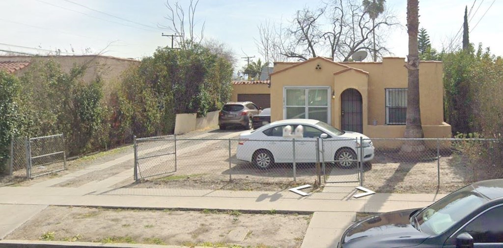 A white car is parked in front of a yellow house.
