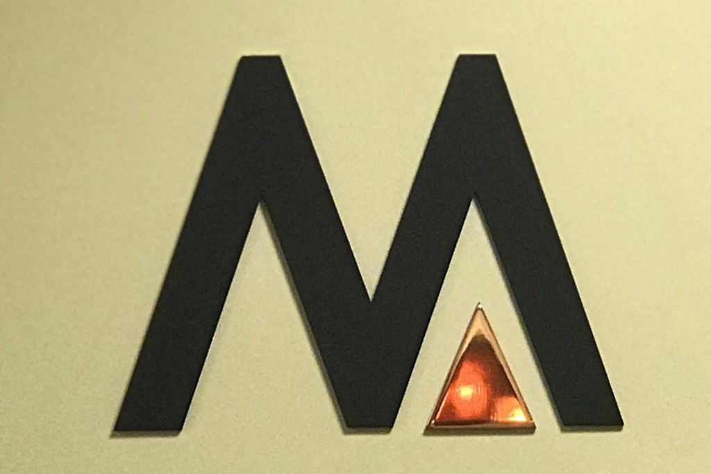 A black letter M with a glowing red triangle in the middle.