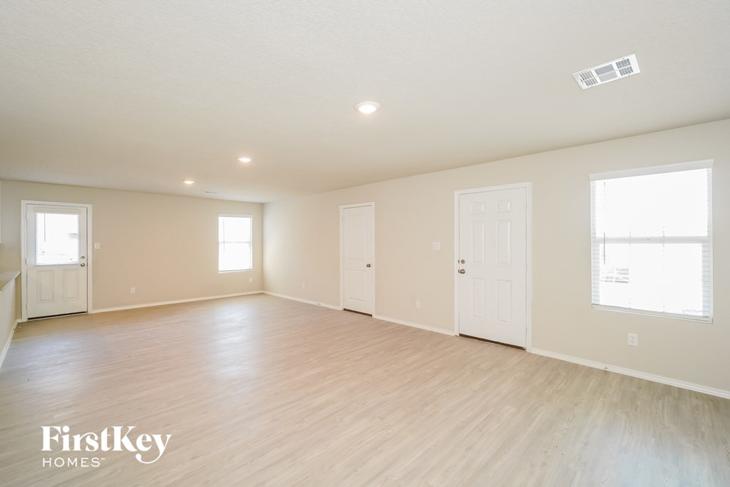 A spacious empty room with wooden flooring and white walls.