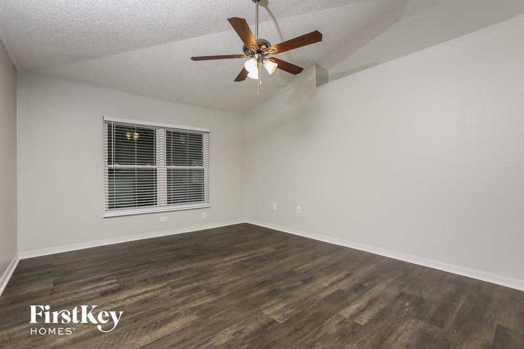 the spacious living room with hardwood flooring and a ceiling fan