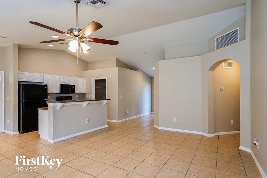 A spacious kitchen and living room with a ceiling fan and beige walls.