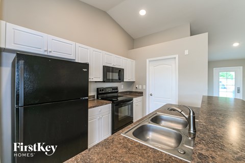 A kitchen with a black fridge and a sink with two faucets.