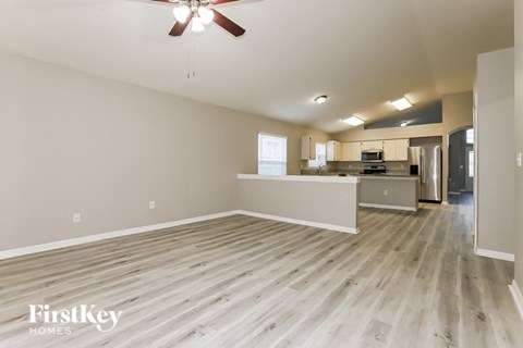 an empty living room and kitchen with wood flooring and a ceiling fan