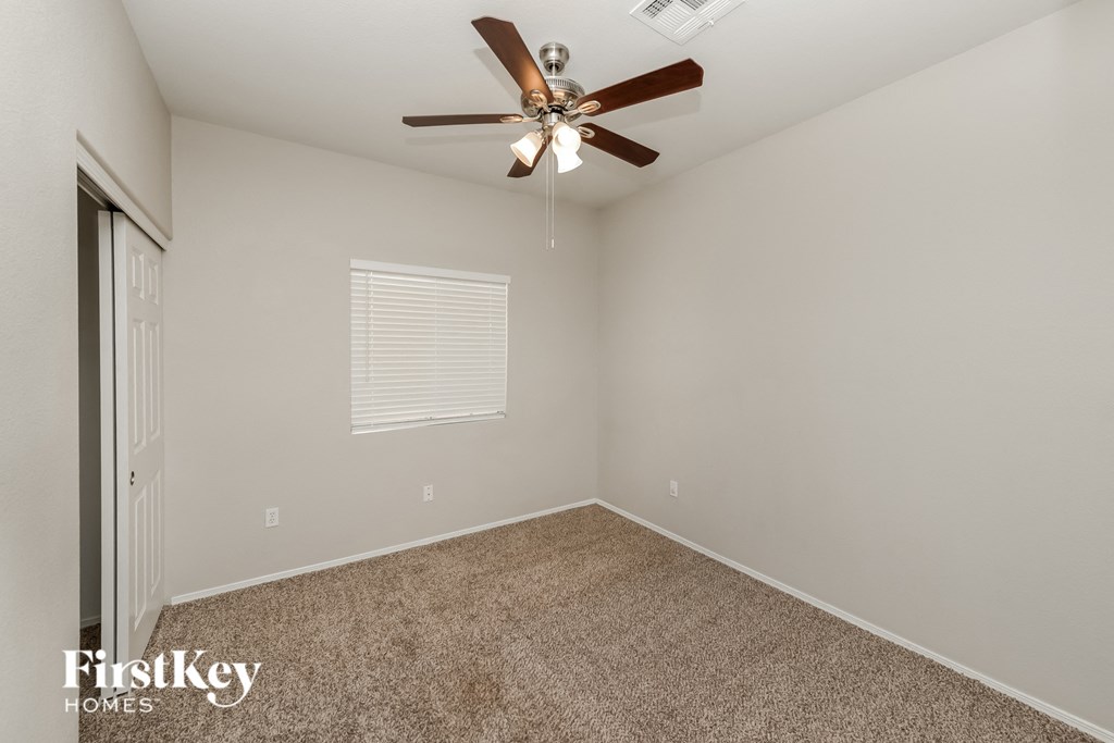 the spacious bedroom has a ceiling fan and beige carpet