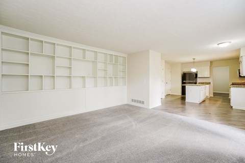 an empty living room with white shelves and a kitchen