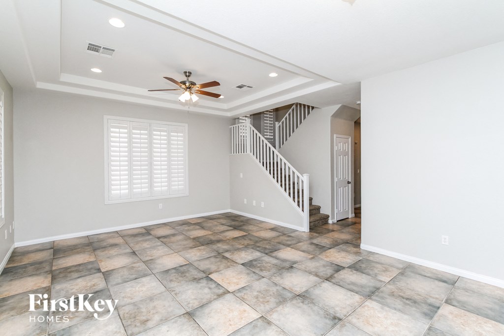 an empty living room with a ceiling fan and a staircase