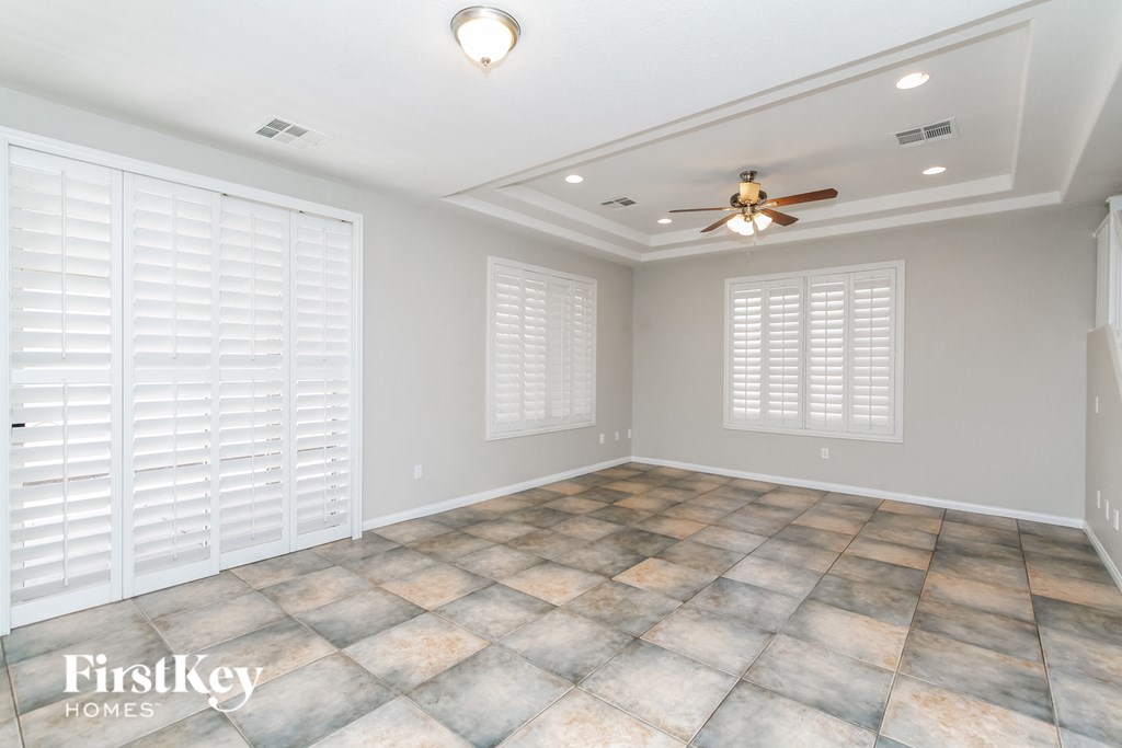 an empty living room with a ceiling fan and shuttered windows