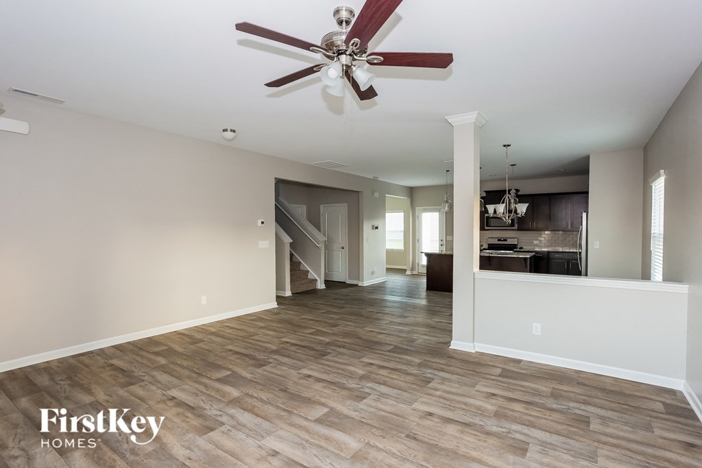 an empty living room with a ceiling fan and a kitchen