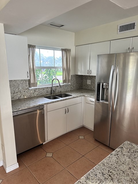 A kitchen with a stainless steel refrigerator and a granite countertop.