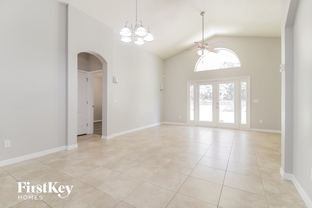 an empty living room with a large tiled floor and a door to the kitchen