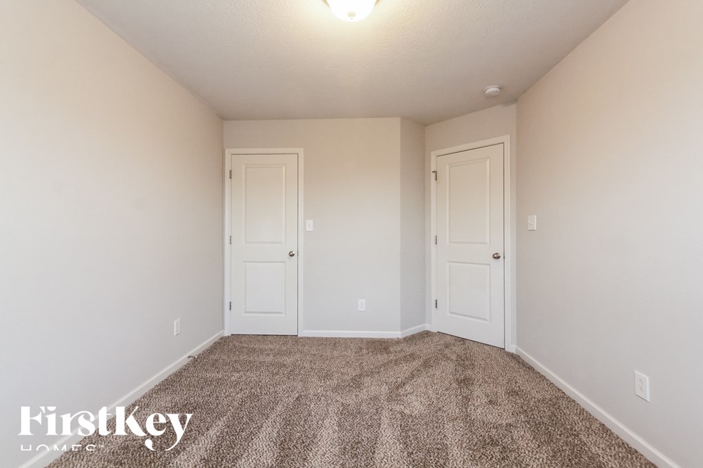 A carpeted room with two doors and a light on the ceiling.