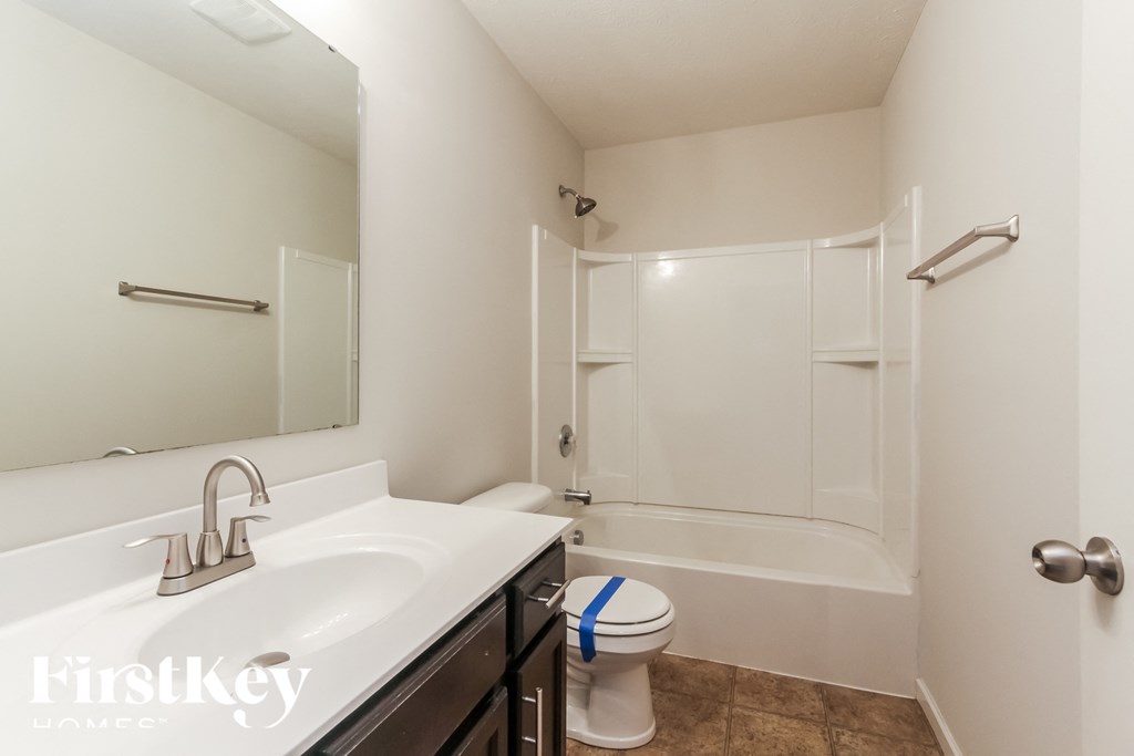A white toilet with a blue stripe on the lid is in a bathroom with a white sink and a walk-in shower.