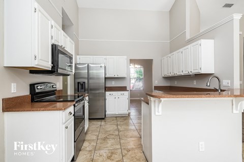 A kitchen with white cabinets and appliances, and a brown countertop.