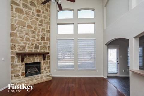 A stone fireplace in a room with a wood floor and a ceiling fan.