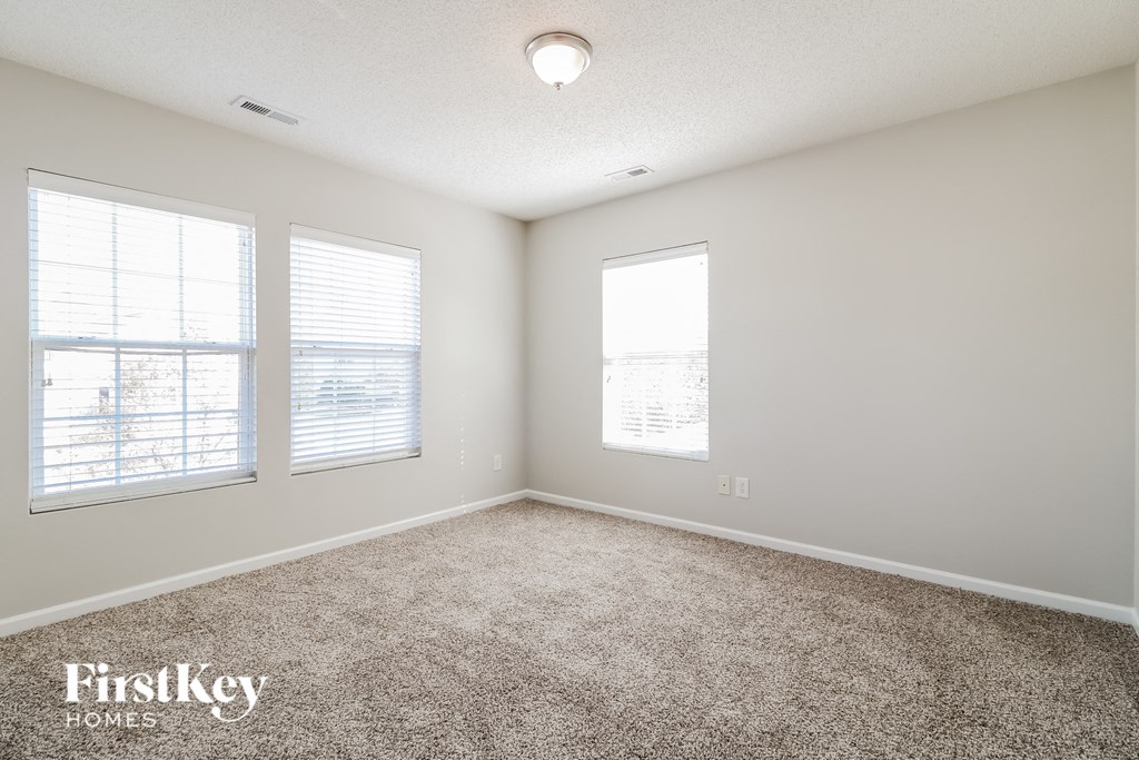 a spacious living room with carpet and three windows