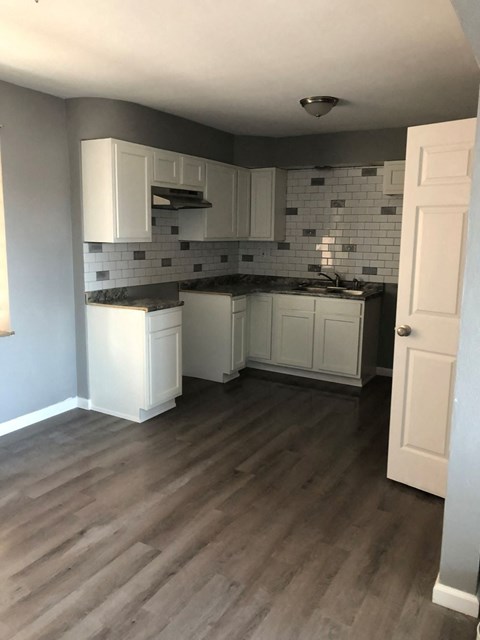 a small kitchen with white cabinets and a wooden floor