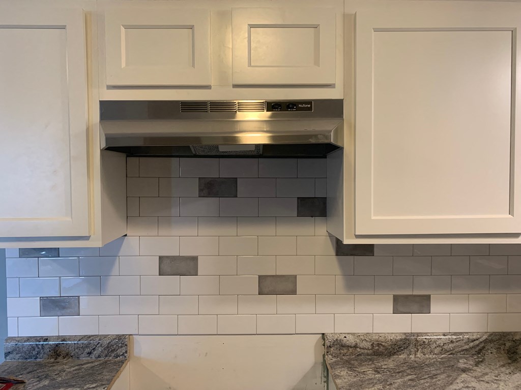 a kitchen with white cabinets and a microwave above a tiled wall