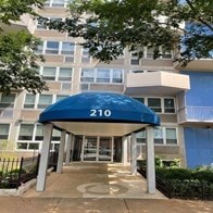 The entrance to apartment building 210 is covered by a blue awning.