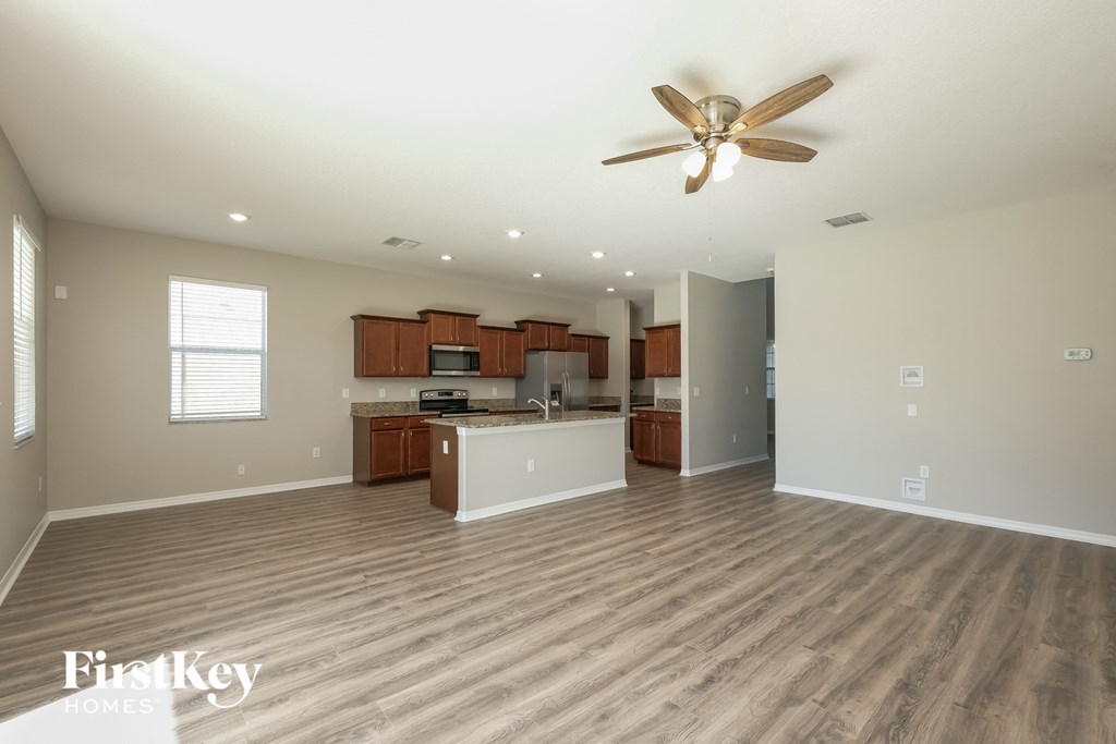 an empty living room with a ceiling fan and a kitchen