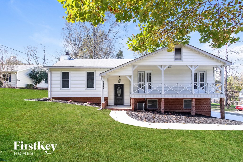 A white house with a porch and a brick wall.