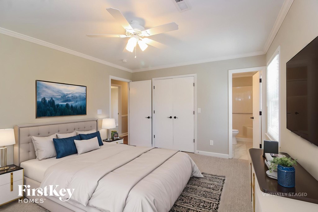 A bedroom with a large bed, a ceiling fan, and a painting on the wall.