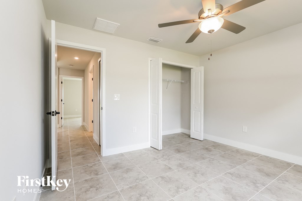 a master bedroom with a ceiling fan and a hallway to two closets