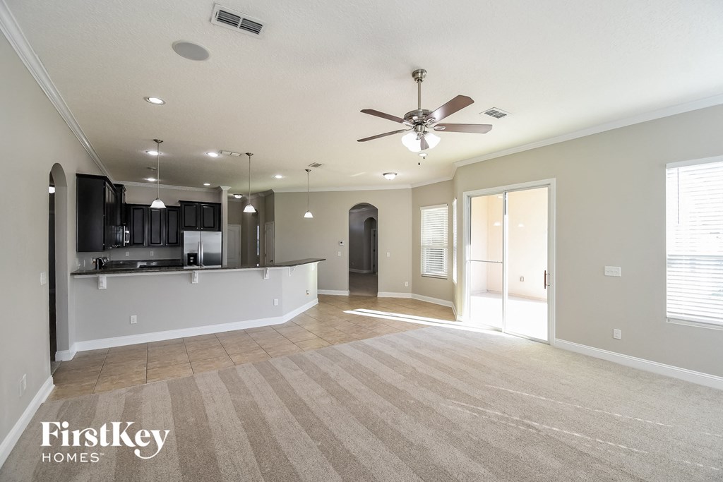 an empty living room with a ceiling fan and a kitchen