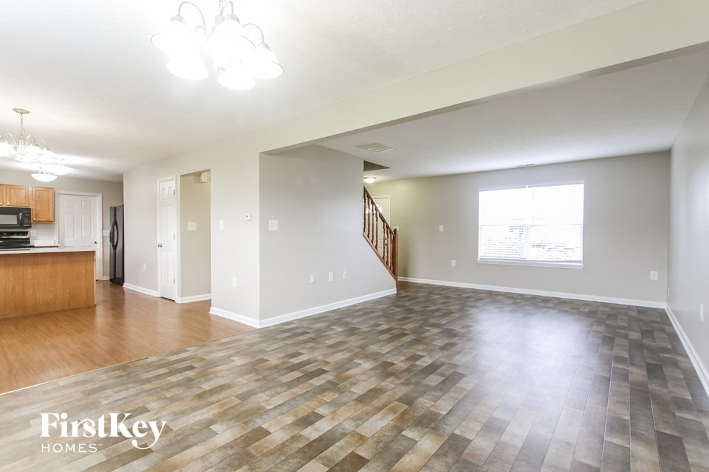 A spacious living room with a checkered floor and a staircase in the background.