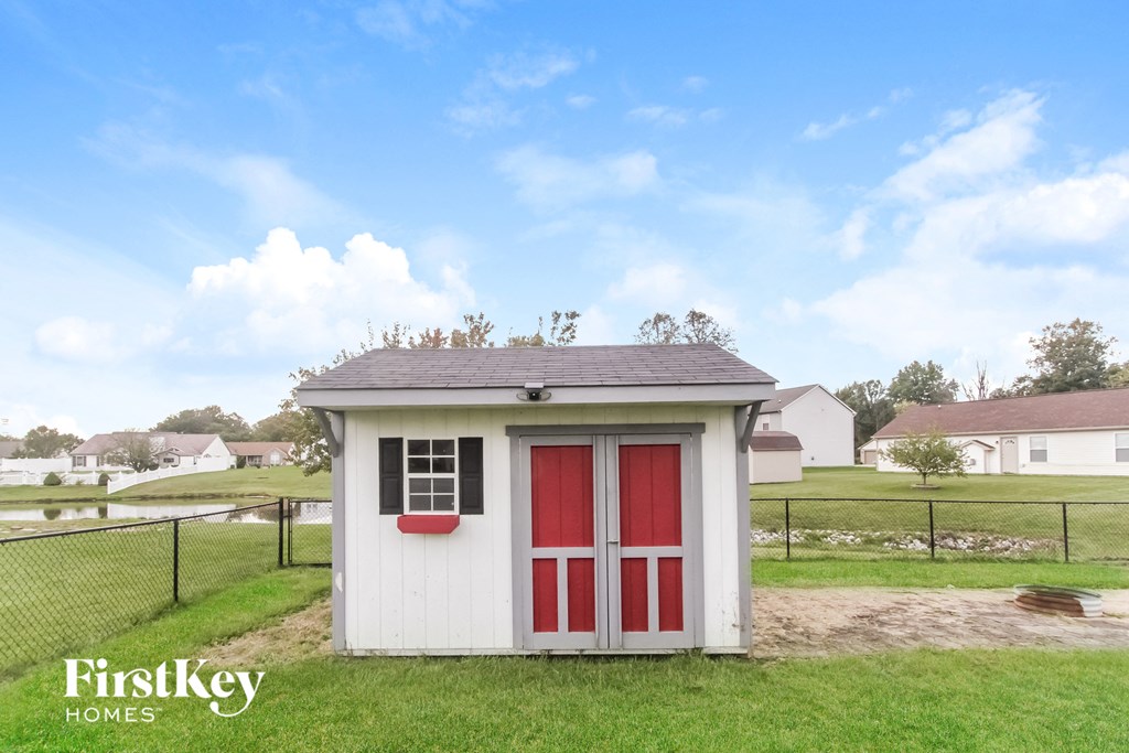 A small white shed with a red door stands in a grassy field.