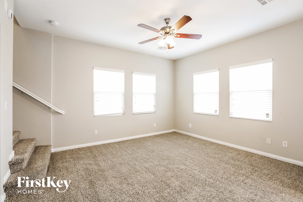 an empty living room with a ceiling fan and three windows