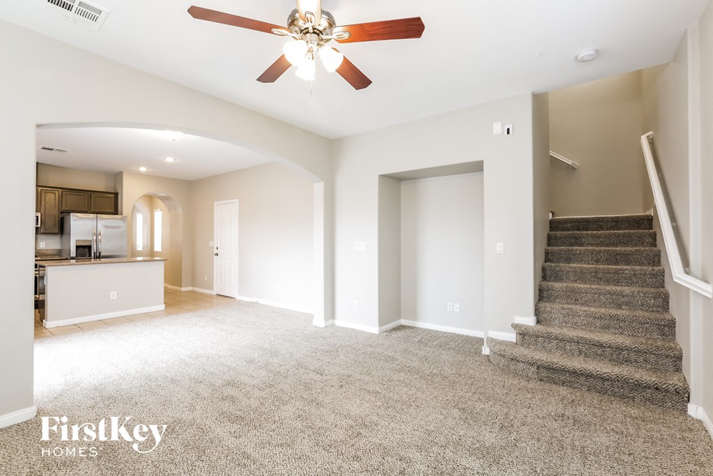 an empty living room with stairs and a ceiling fan