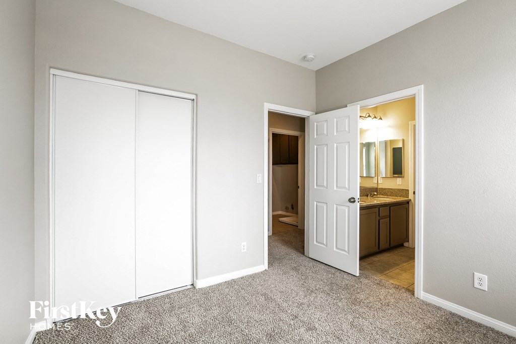 a bedroom with a closet and a bathroom with a sink and a mirror