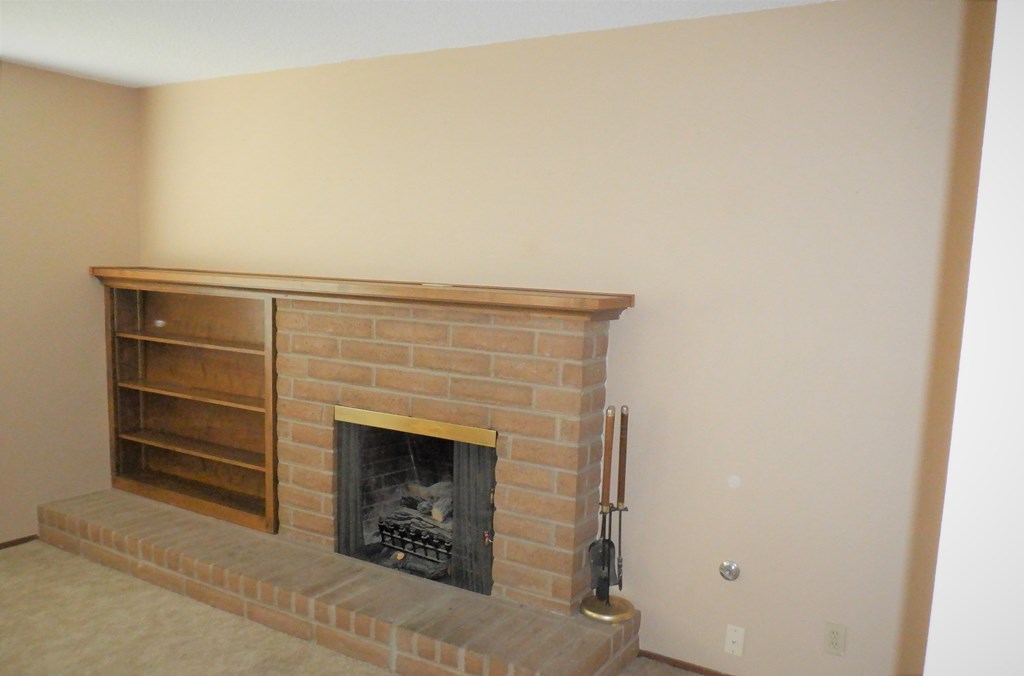 the living room has a brick fireplace and a book shelf