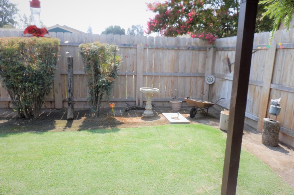 a backyard with a wooden fence and a bird bath in the grass