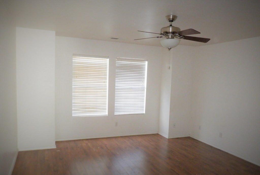 an empty living room with a ceiling fan and two windows