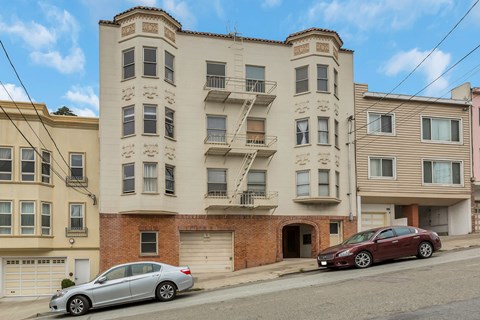 A row of apartment buildings with cars parked in front.