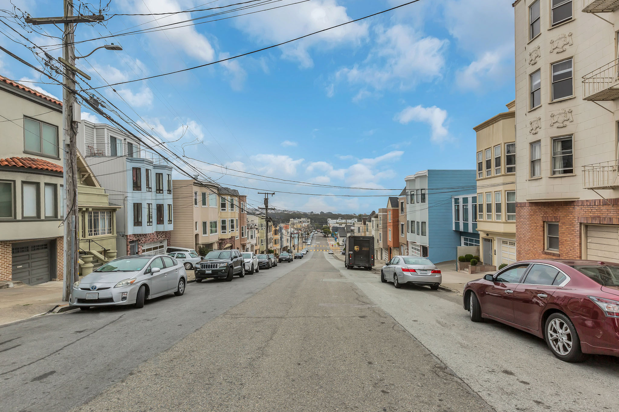 A street with cars parked on both sides and buildings on the sides.