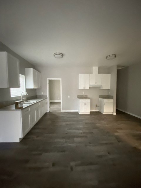 an empty kitchen with white cabinets and a wooden floor