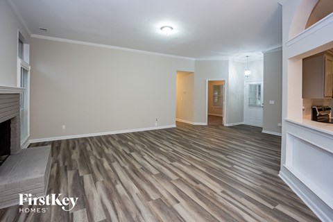 A spacious room with wooden flooring and a fireplace on the left side.