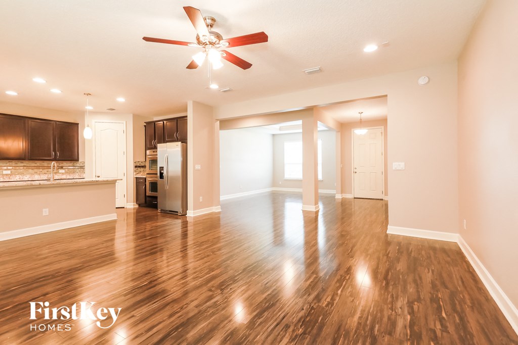 an empty living room with a ceiling fan and a kitchen