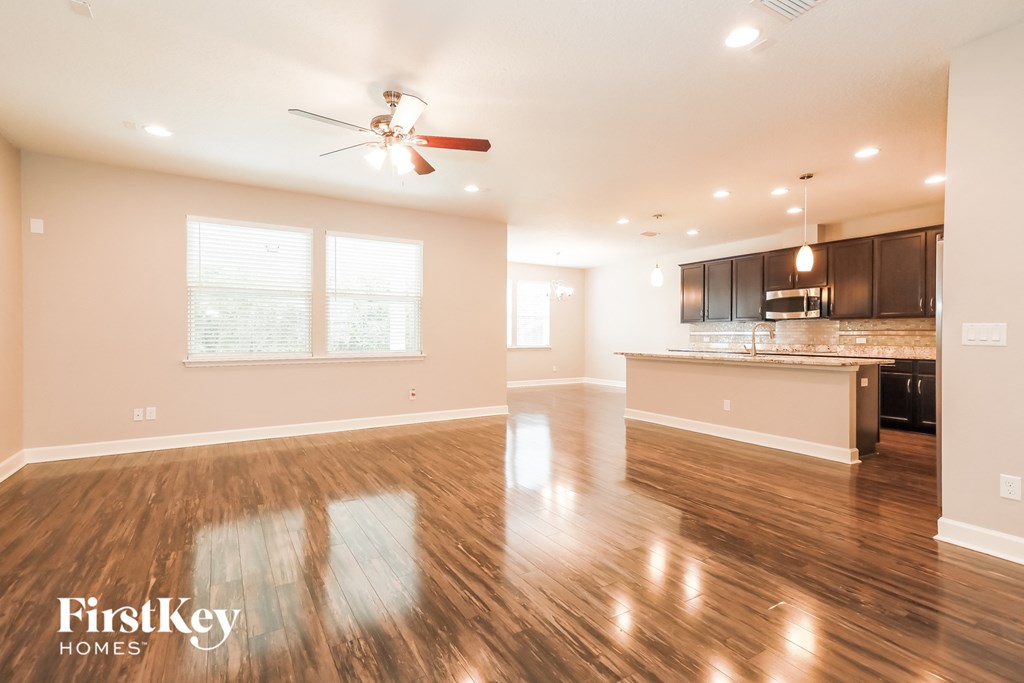 an empty living room and kitchen with wood flooring and a ceiling fan