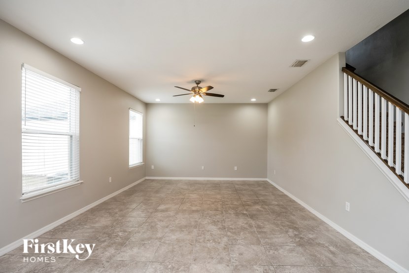 A spacious room with a ceiling fan and a staircase on the right side.